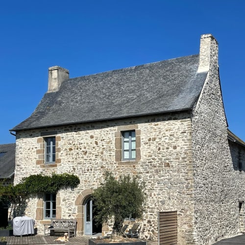 Stone manor house exterior in Val d'Izé with slate roof, chimneys, and manicured garden entrance
