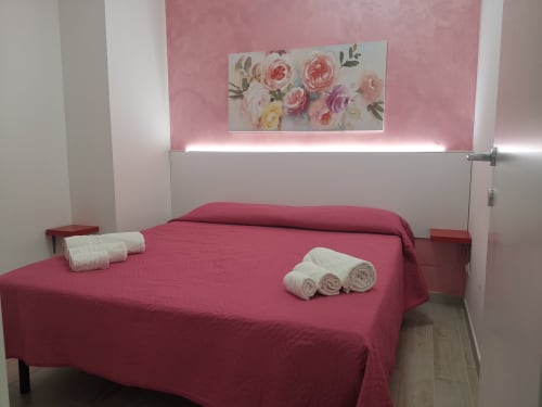 Camera da letto in stile spa moderno con letto cremisi, asciugamani bianchi e opere floreali a Casa Vacanze Del Golfo a Castellammare del