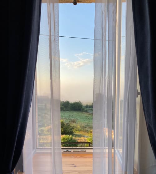 Portes-fenêtres ouvertes à La Maison De Fleurat offrant une vue sur le jardin et la campagne de Domeyrot avec ses champs verdoyants et ciel bleu