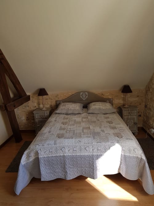Chambre cosy sous les toits aux Granges Indigo B&B à Fossemagne avec plafond aux poutres apparentes, lit matelassé et planchers de bois chaud.