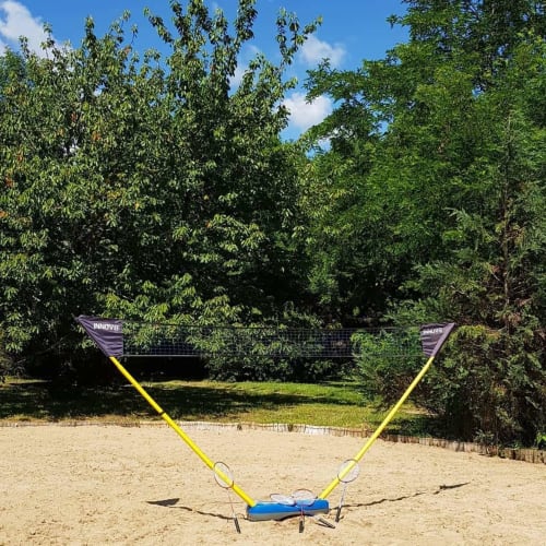 Filet de badminton installé sur la plage de sable aux Granges Indigo, Fossemagne, avec verdure luxuriante en arrière-plan