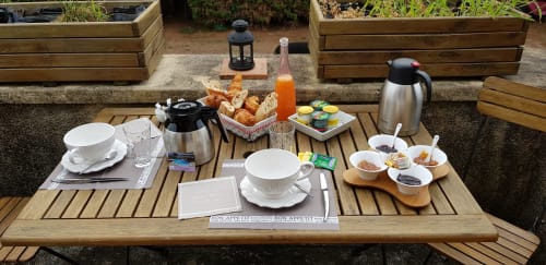 Outdoor breakfast spread at Les Granges Indigo B&B with pastries, orange juice, coffee and jam at wooden table.