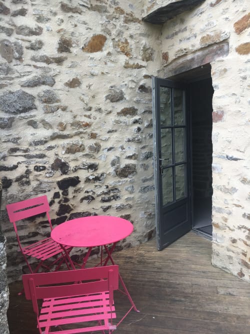 Pink bistro chairs and table on wooden deck against historic stone walls at Manoir de la Nogrie, France