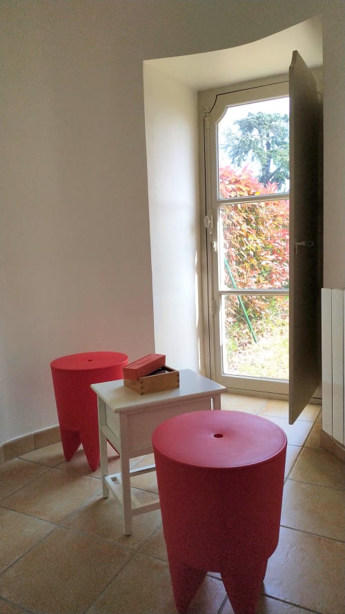 Modern sitting area with red cylindrical furniture and white desk overlooking garden at Locacharme cottage in Blois