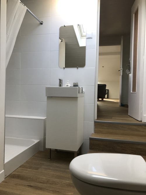 Salle de bains moderne avec carrelage blanc, lavabo sur pied, miroir et parquet aux Gîtes De L'odet