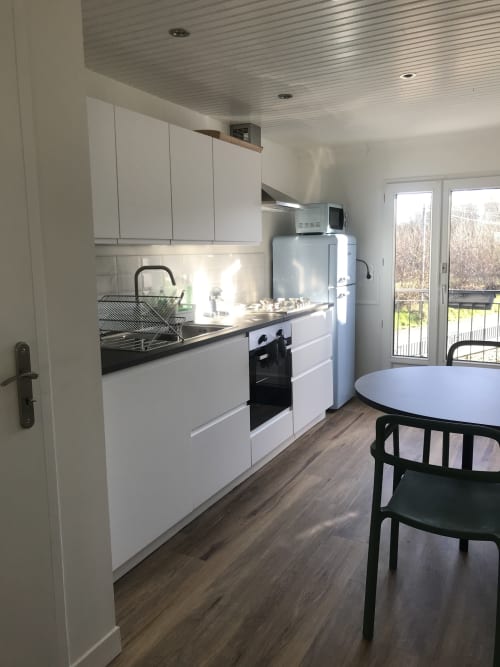 Cuisine moderne blanche avec plan de travail noir, électroménagers inox, coin repas et vue sur le jardin aux Gîtes De L'odet