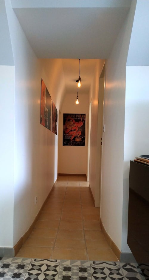 Modern hallway at Locacharme cottage in Blois with warm lighting, white walls, terracotta tiles, and vintage posters