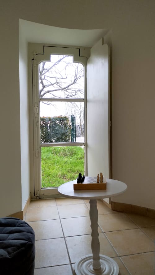 Bright sunlit interior of Gîte Auguste Poulain in Blois with round table, tall window overlooking green garden and bare trees