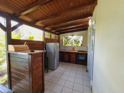 Open kitchen with wooden cabinetry, stainless steel refrigerator, and gas cooktop in Lewoz apartment at Gites Kaladja,