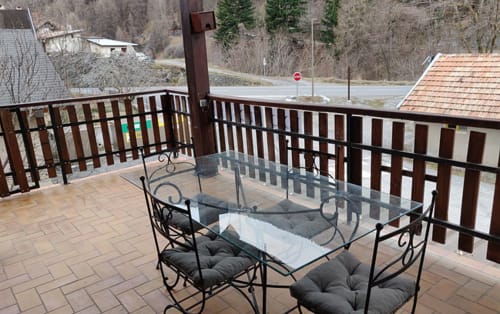 Balcon avec vue sur la montagne à l'hôtel Location MarjoRI, table à manger en verre et chaises noires surplombant la vallée du Lauzet-Ubaye