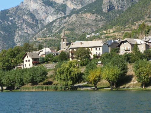 Le charmant village alpin de Le Lauzet-Ubaye avec son église, ses bâtiments au bord du lac et ses majestueuses montagnes