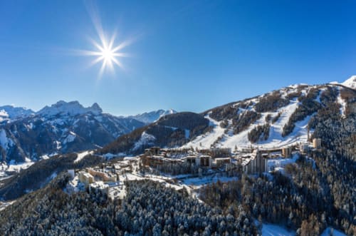 Station de montagne enneigée à Le Lauzet-Ubaye : pistes de ski, forêt alpine et ciel bleu ensoleillé