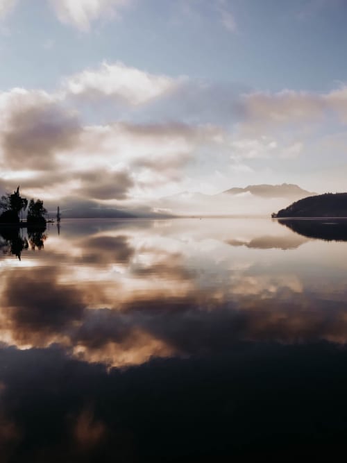 Reflex serè del llac a la sortida del sol amb muntanyes nebuloses, Le Manoir Lacustre, Queyrac