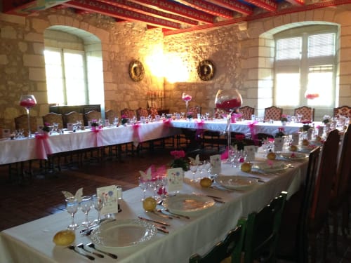Elegant banquet hall at Château de Ré with white-draped tables, pink floral arrangements, and stone archway in Le Petit