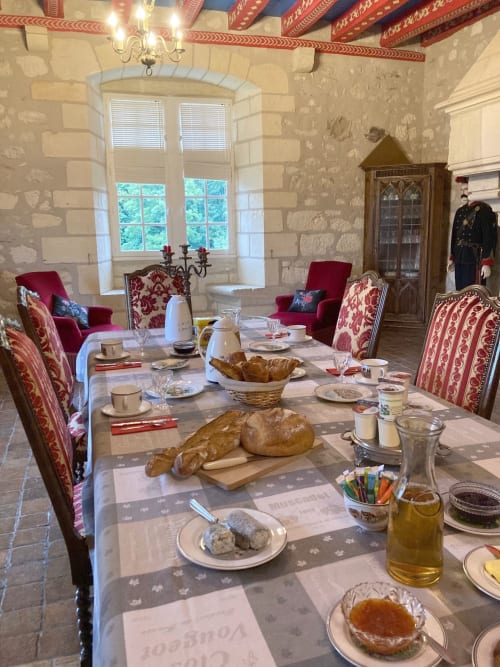 Salle à manger élégante du Château de Ré avec mobilier d'époque, pain frais et chaises damassées rouges