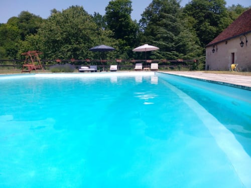 Crystal clear swimming pool at Château de Ré boutique hotel in Le Petit Pressigny, France, with umbrellas and lounge chairs