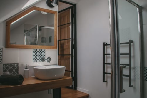 Salle de bains moderne aux Chambres d'hôtes Saint Jean avec vasque ronde blanche, meuble en bois, carrelage à motifs et sèche-serviettes noir