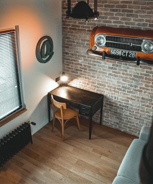 Espace de travail moderne aux Chambres d'hôtes Saint Jean avec art vintage de voiture orange sur mur de brique, bureau, chaise en bois et ambiance