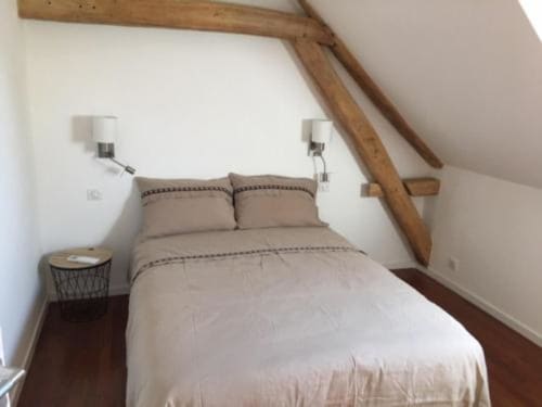 Chambre sous les toits cosy aux Portes De Bourgogne avec poutres apparentes, linge de lit crème et appliques murales à Serbonnes.