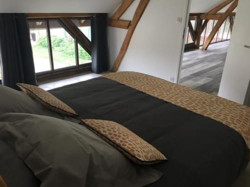 Chambre moderne aux Portes De Bourgogne : literie noire, coussins à motifs, poutres apparentes, vue sur jardin