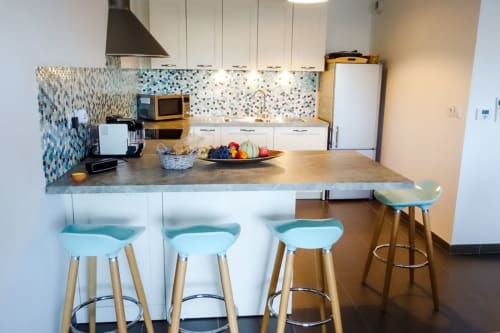 Cuisine moderne avec tabourets bleus turquoise, dosseret en mosaïque, armoires blanches et plan de travail en granit dans un appartement provençal