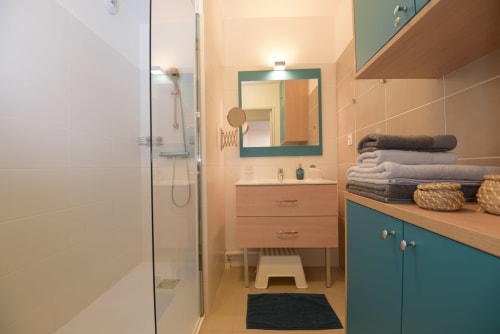 Salle de bain moderne de l'appartement Ô de Mer C à La Cadière d'Azur, avec accents bleu-vert, douche à l'italienne, vasque et miroir