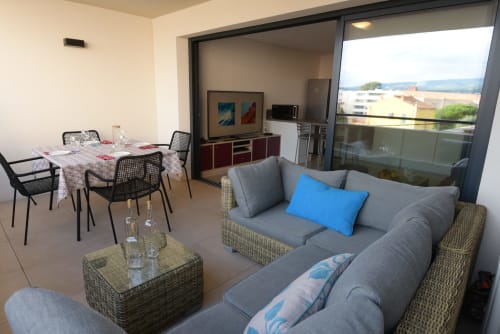 Salon moderne d'appartement avec canapé gris, coin repas et balcon surplombant la campagne de La Cadière d'Azur, Provence