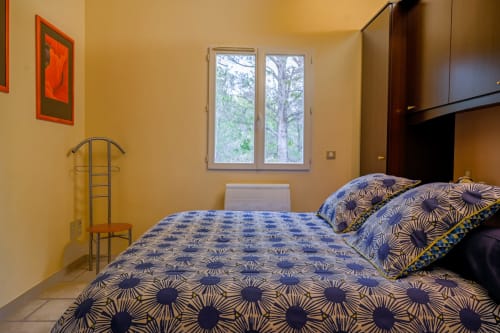 Chambre jaune ensoleillée en Provence avec literie motifs bleus, vue sur le jardin par fenêtres doubles, équipements modernes