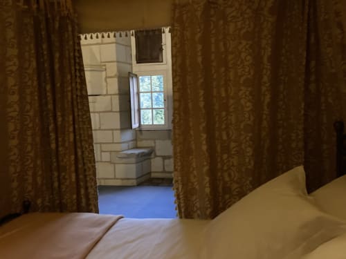 Chambre d'Aliénor d'Aquitaine au Château de Ré avec vue sur le jardin, literie crème, rideaux dorés et salle de bain en tour de pierre