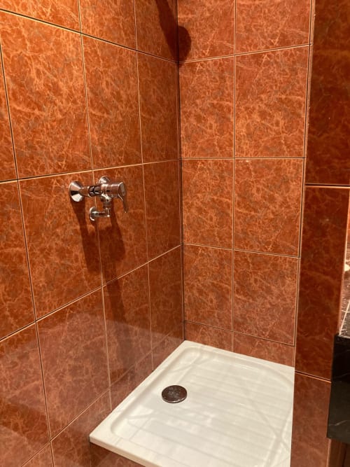 Salle de douche moderne aux carreaux de marbre rouge-rouille et robinetterie chromée au Château de Ré, hôtel boutique du Petit Pressigny
