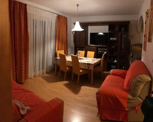Open-plan living and dining area in Giustina Apartment, Gargazzone with red armchairs, dining table, and entertainment unit