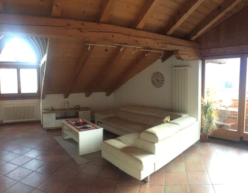 Spacious attic apartment living room with exposed beams, white seating, kitchenette, and mountain views in Gargazzone