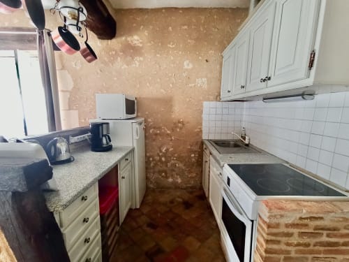 Kitchen at Château de Ré B&B in Le Petit Pressigny with white cabinets, stovetop, and damaged beige walls.