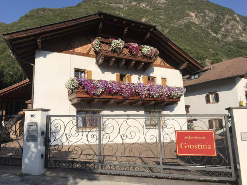 Appartamento Giustina mit violetten Blütenbalkönen, Gargazzone-Bergblick und verziertem Eingangstor