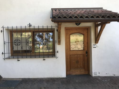 Ground floor entrance of Appartamento Giustina in Gargazzone with wooden door, barred window, and tiled roof overhang