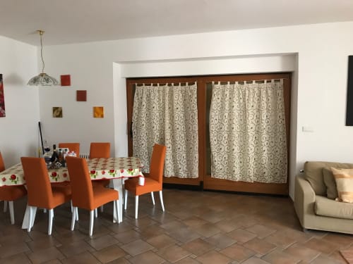 Bright dining and living area in ground floor apartment with orange chairs, patterned curtains, and beige sofa at