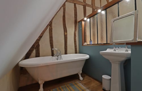 Salle de bain charmante à La Dragonne B&B à Bellême avec baignoire îlot, lavabo sur colonne et poutres apparentes