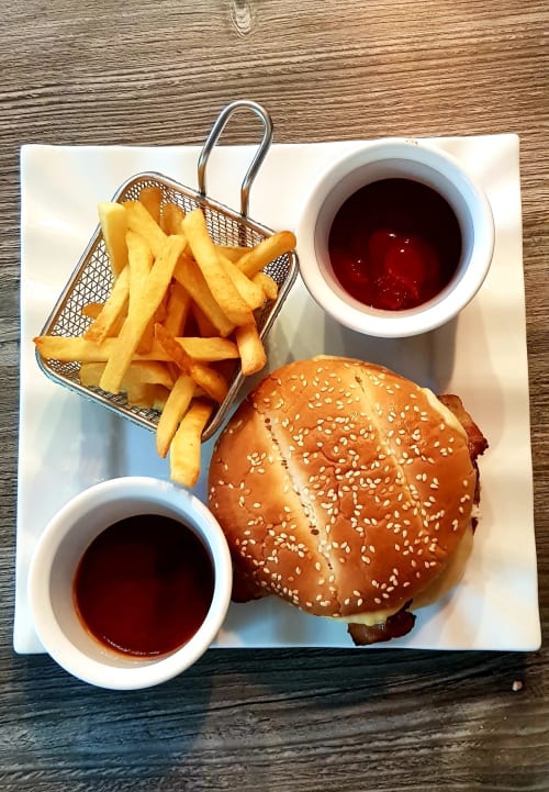 Burger with sesame bun, crispy fries in basket, and two sauce bowls at Les Granges Indigo, Fossemagne