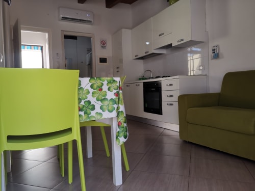 Modern apartment kitchen and living area with lime green chairs, white cabinetry, and olive sofa at Casa Vacanze Del Golfo,