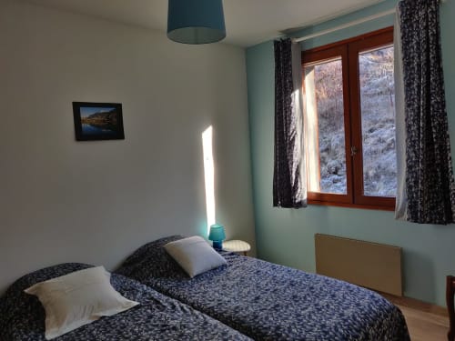 Chambre cosy d'appartement montagnard avec lits jumeaux, murs bleu-canard et vue sur les Alpes enneigées à l'hôtel Marjo RI