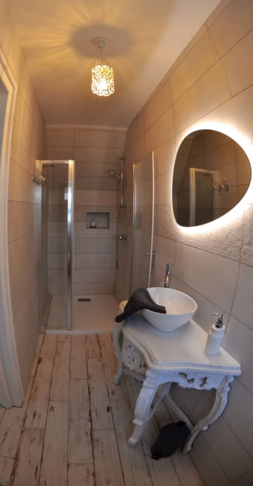 Modern bathroom at Aux Prés Du Berry with illuminated round mirror, walk-in shower, and decorative white sink vanity