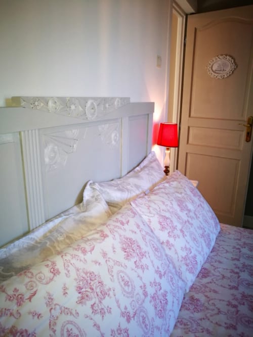 Cozy bedroom at Aux Prés Du Berry B&B with pink floral bedding, ornate white headboard, and red bedside lamp