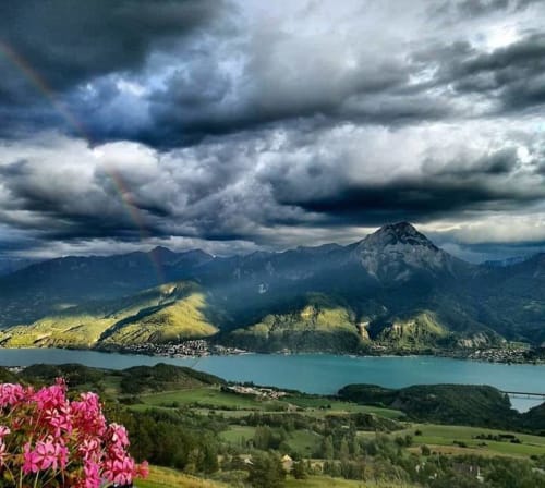 Vallée alpine aux nuages dramatiques, montagnes majestueuses et fleurs roses près du Lauzet-Ubaye