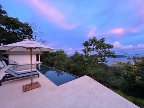 Lodge de luxe à Paquera avec piscine à débordement face à l'océan Pacifique au coucher du soleil, parasol et chaises longues sur la terrasse