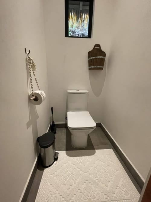 Salle de bains moderne du refuge Organica Yoga avec toilettes blanches, paniers tressés en bois et décoration minimaliste.