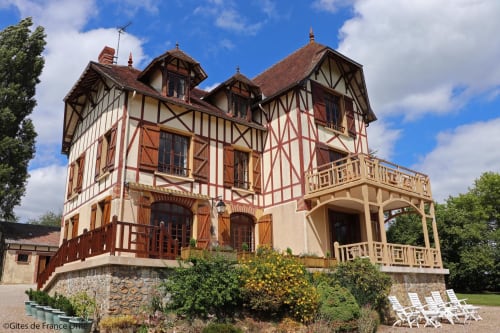 Vue depuis le jardin de la maison avec colombages en trompe l'œil, salon de jardin et massif de fleurs Domaine des Thomins Maison d'hôte Cisai Saint-Aubin Hôtel Gacé