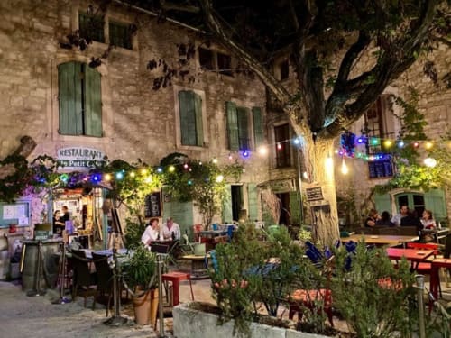 Avondplaats bij Provence Km28 in Gordes met stenen gebouwen, glinsterende verlichting, eettafels en grote boom