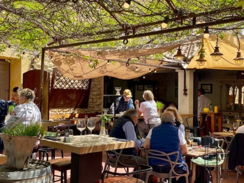 Buitenterras voor dineren bij Provence Km28 B&B in Gordes met gasten, wijnranken en gezellige bistro-sfeer