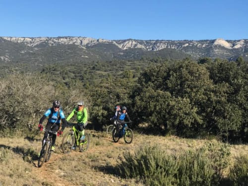 Trois vttistes sur sentier avec vue sur la campagne de Gordes, oliverais et falaises calcaires