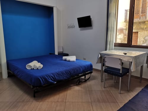 Studio Blu apartment bedroom with blue bed, desk, and city view window at Casa Vacanze Del Golfo, Castellammare del Golfo